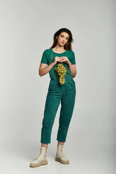 A young woman in a green outfit holds a bunch of grapes. — Stock Photo