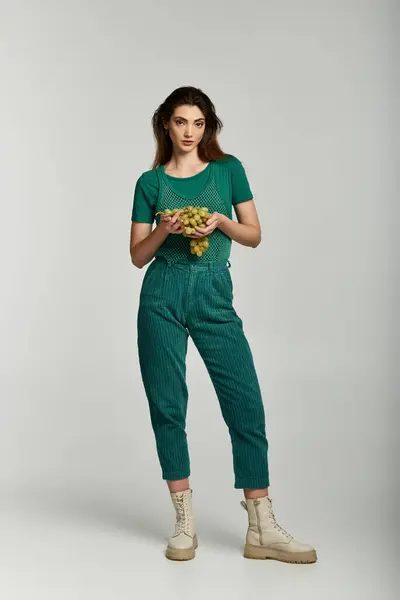 A young woman in a green outfit holds a bunch of grapes in a studio setting. — Stock Photo