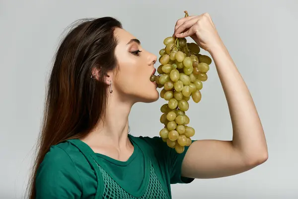 A young woman in a green shirt savors a juicy bunch of grapes. — Stock Photo