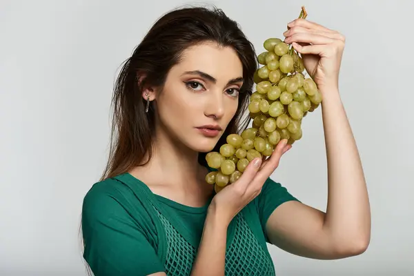 A young woman in a green top holds a bunch of green grapes. — Stock Photo