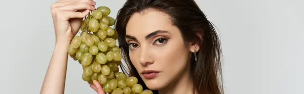A young woman in elegant attire holds a bunch of green grapes. — Stock Photo