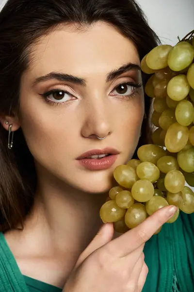 A young woman with elegant attire holds a bunch of grapes near her face. — Stock Photo