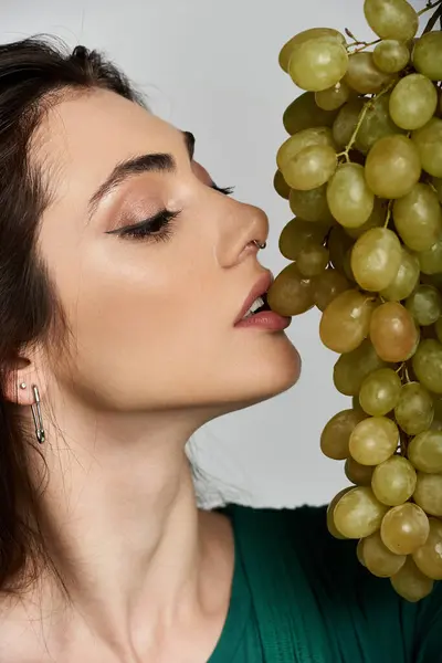 A beautiful woman in an elegant green dress savors the taste of a juicy grape. — Stock Photo