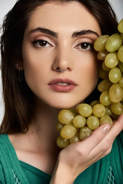 Close-up of young woman with long hair, green dress, grapes. — Stock Photo