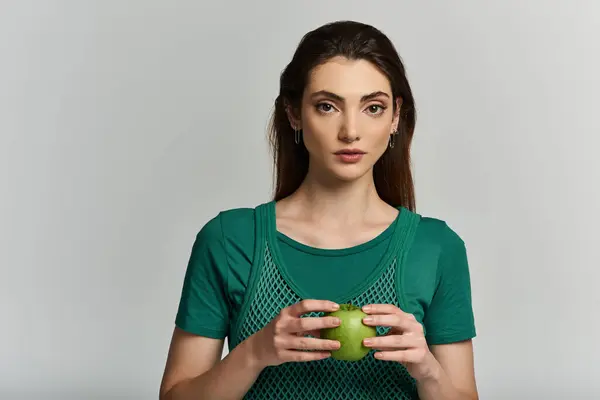 Una joven vestida de verde sostiene una fruta verde inmadura. - foto de stock