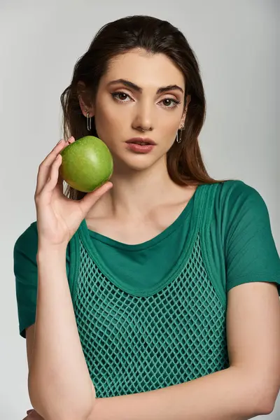 A young woman in a green, mesh top holds a green apple against her cheek. — Stock Photo