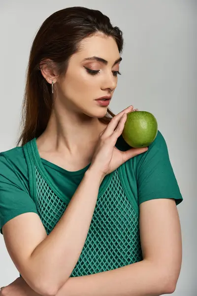 A young woman in a green top holds an apple. — Stock Photo