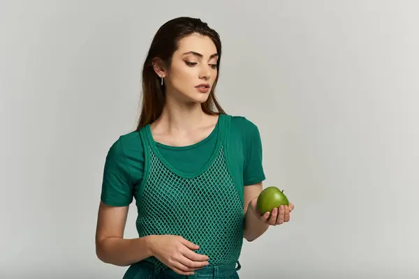 A young woman in a green mesh top holds a green apple, looking down at it thoughtfully. — Stock Photo