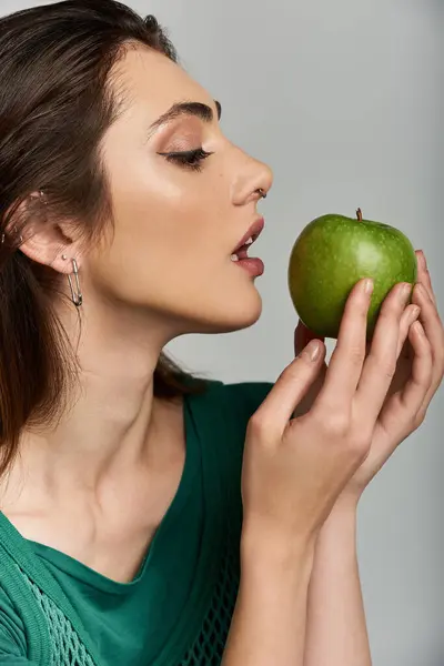 A young woman in a green shirt gazes at a green apple held in her hands. — Stock Photo