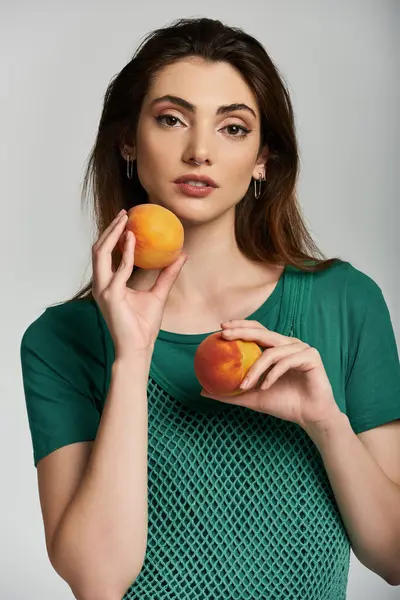 Uma jovem de camisa verde segura dois pêssegos maduros. — Fotografia de Stock