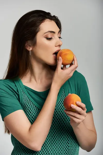 A young woman in a green mesh top takes a bite of a peach. — Stock Photo