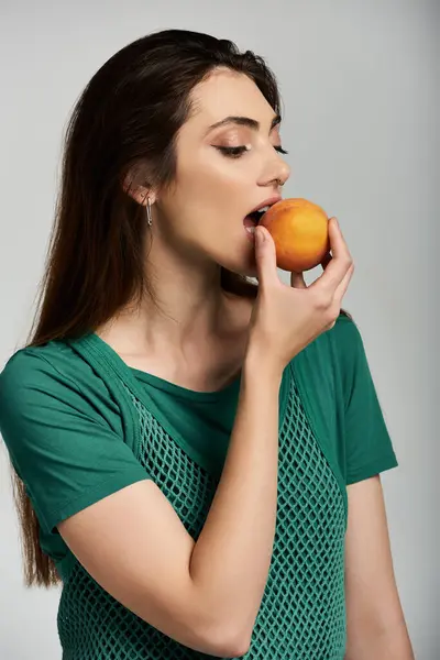 A young woman in a green shirt bites into a peach. — Stock Photo