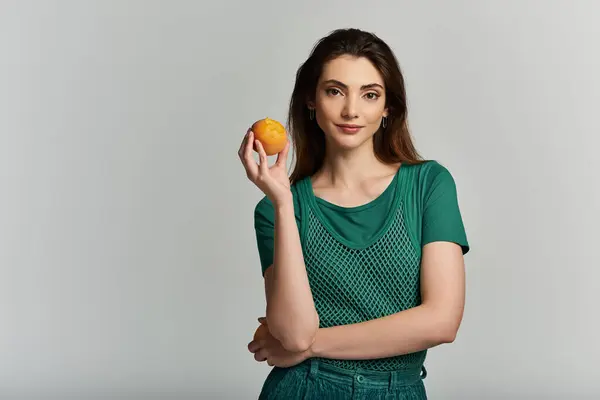 A young woman in a green shirt holds a bright orange fruit. — Stock Photo