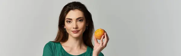 A young woman in an emerald green top holds a peach and smiles at the camera. — Stock Photo