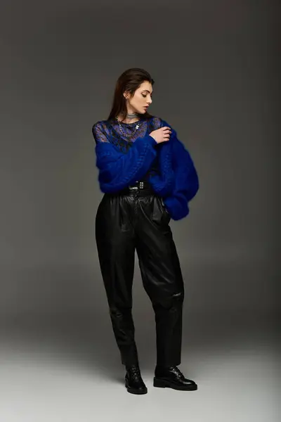 A young woman stands in a studio setting wearing a blue fuzzy knitwear and black leather pants. — Stock Photo