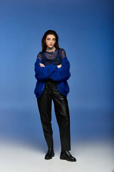 A young woman stands confidently in elegant attire against a blue backdrop. — Stock Photo