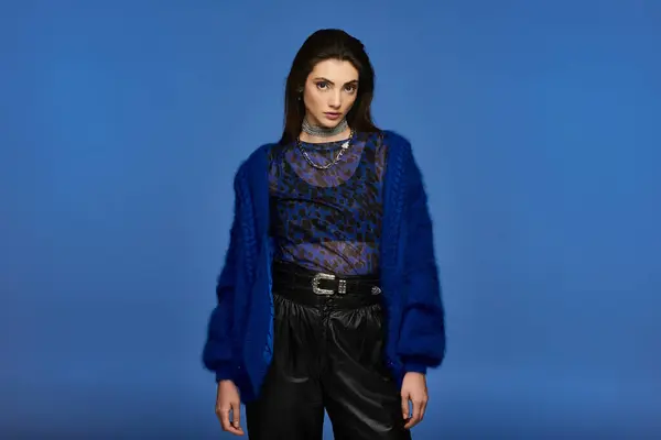 A young woman in a blue cardigan and black pants, posing against a blue backdrop. — Stock Photo