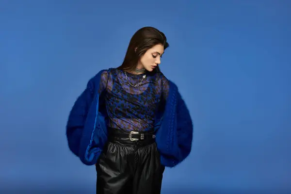 A young woman in a blue fuzzy jacket poses against a solid blue background. — Stock Photo