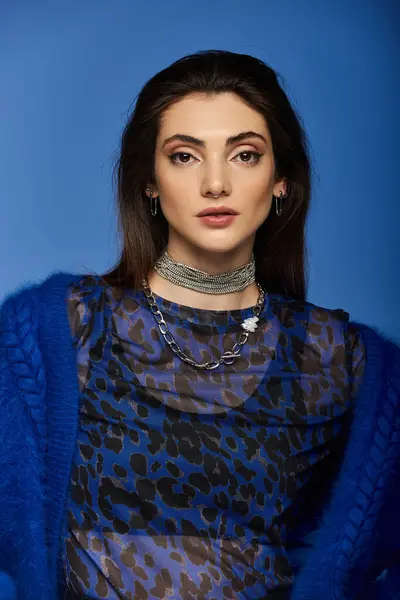 Young woman with dark hair in blue mesh top and chains poses on blue background. — Stock Photo