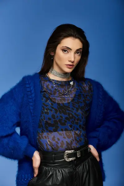 A young woman in a blue cardigan and a leopard-print top stands against a bright blue background. — Stock Photo