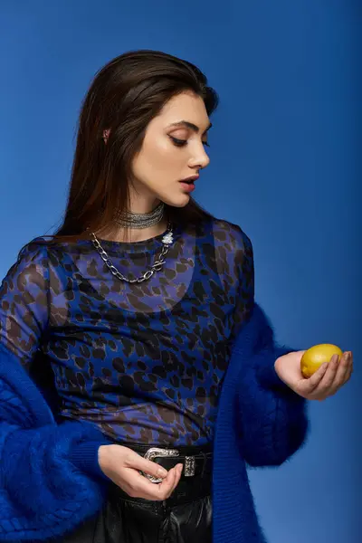 A young woman in a blue patterned top holds a lemon against a blue background. — Stock Photo