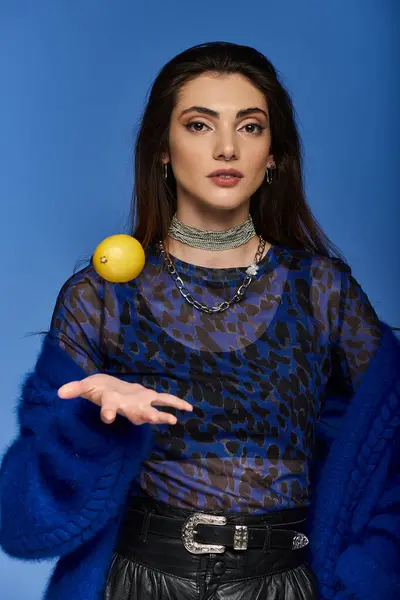A young woman in elegant attire poses with a lemon in front of a blue background. — Stock Photo