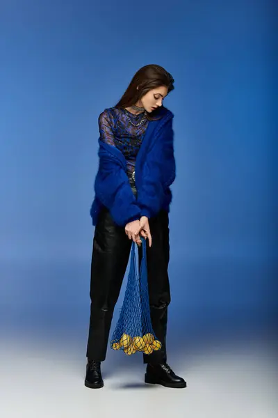 Young woman in blue dress poses with net bag of fruit against blue backdrop. — Stock Photo