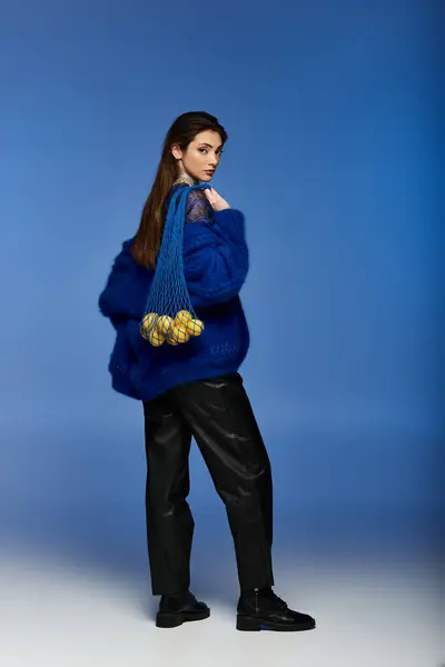 A young woman in a blue fuzzy jacket and black pants stands against a blue backdrop. — Stock Photo
