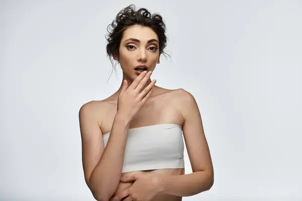 A young woman in a white top looks surprised and covers her mouth with her hand. — Stock Photo