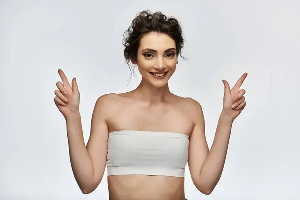 A young woman in a white strapless top smiles and points with both hands. — Stock Photo
