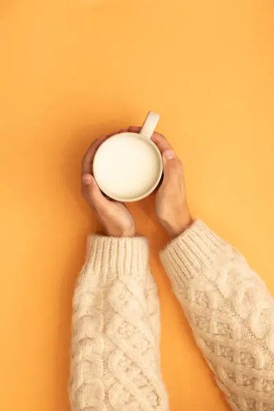 hands grabbing milk mug woolen sweater