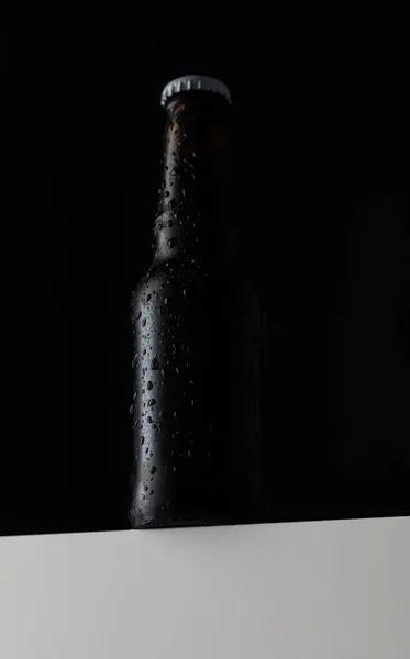 small Beer bottle with water drops in black background, white cap, seen from below