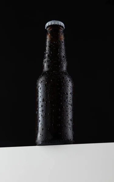 small Beer bottle with water drops in black background, white cap, seen from below