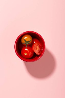 Domatesler kasenin üstünde pembe arka planda.