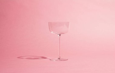 Yumuşak pembe arka planda boş bir cam kadehin minimalist görüntüsü. Basit ve zarif kompozisyon içki temaları, tarz ve modern tasarım için mükemmeldir..