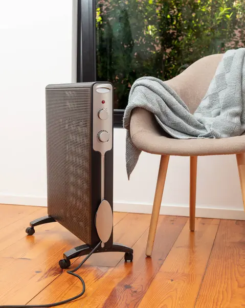 Pürüzsüz, modern elektrikli ısıtıcı battaniyeli rahat bir sandalyenin yanına yerleştirilmiş şık bir evin içinde, ahşap bir zemine kurulmuş. Mekanını sıcak ve rahat tutmak için mükemmel..