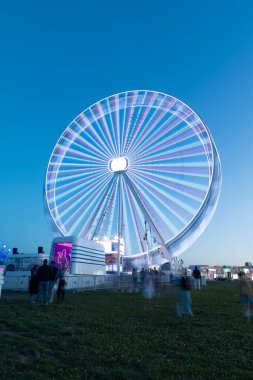 A stunning long exposure shot of a brightly lit Ferris wheel at Rock in Rio Lisboa 2024. The vibrant lights and motion blur create a mesmerizing effect, capturing the festive atmosphere of the night. clipart