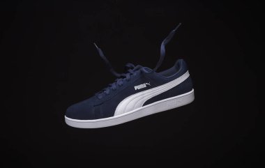 Puma spor ayakkabılarının siyah arka planda asılı olduğu dinamik bir stüdyo çekimi beyaz çizgili lacivert tasarımı vurguluyor. Modern spor ayakkabılarını, stilini ve markasını sergilemek için mükemmel..