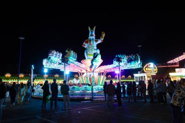 Bir lunaparkta canlı bir gece sahnesi. Etrafı insanlarla çevrili renkli, aydınlık bir kanguru gezisi. Parlayan ışıklar ve şenlikli atmosfer karnavalın heyecanını ve eğlencesini yakalıyor..