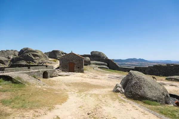 stock image The image shows a historic chapel with an orange roof located at the top of the Monsanto Castle in Portugal. The stone structure stands out against the rocky landscape, surrounded by a clear blue sky.