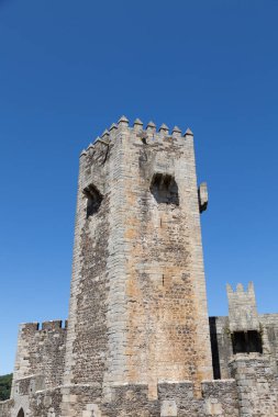 Portekiz 'deki Sabugal Kalesi' nde, ortaçağ mimarisini sergileyen heybetli taş duvarlar ve tarihi bir taş merdiven bulunuyor. Görüntü, açık mavi gökyüzünün altındaki kaleyi yakalıyor.