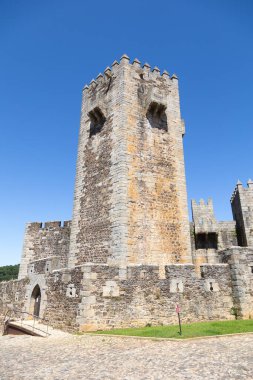 Portekiz 'deki Sabugal Kalesi' nde, ortaçağ mimarisini sergileyen heybetli taş duvarlar ve tarihi bir taş merdiven bulunuyor. Görüntü, açık mavi gökyüzünün altındaki kaleyi yakalıyor.