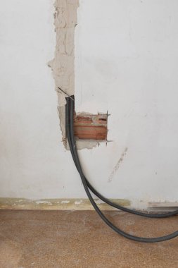 Ev tadilatı sırasında elektrik kablolarıyla korunmasız bir duvar görüntüsü. Bitmemiş alçı ve görünür tuğla sergisi elektrik tesisatına odaklanmış devam eden bir inşaat projesi.
