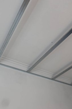 Metal çerçeve ve görünür elektrik kablolarıyla sahte tavan kurulumu devam ediyor. Fotoğraf, bir ev yenileme projesinde tavan inşaatının erken safhalarını gösteriyor. İç inşaat çalışmalarını resimlemek için ideal.