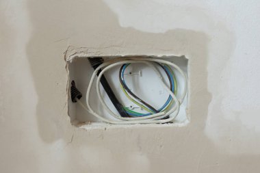 İnşaat alanındaki bitmemiş bir duvardaki elektrik tesisatını ortaya çıkardı. Görüntü kablolar, kanallar ve kısmen sıvanmış bir duvar gösteriyor. Tadilat veya elektrik işleri için ideal..