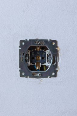 Bitmemiş bir elektrik prizinin, beyaz bir duvara gömülü metal çerçeve ve açıkta kalan kabloları gösteren yakın çekimi. Ev yenileme, elektrik projeleri veya DIY çalışmaları için ideal.