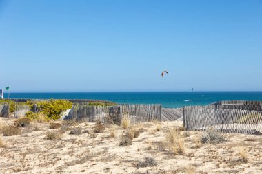 Algarve 'deki Fuseta Adası' nın sakin manzarası. Kum tepecikleri ve uçurtma sörfçüleriyle dolu berrak mavi bir okyanus. Ahşap çitler kırsal bir cazibe katıyor, sahil manzarasına çok güzel uyum sağlıyor..