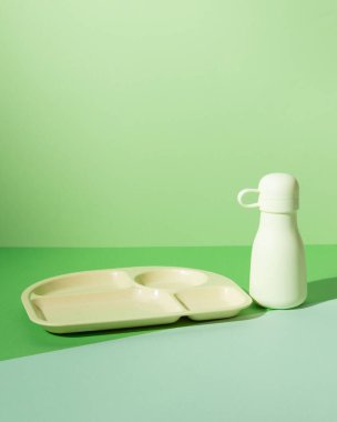 Minimalist çevre dostu yemek tepsisi ve yeşil arka planda yeniden kullanılabilir su şişesi. Bu temiz ve şık görüntü sürdürülebilir yaşam ve sıfır atık ürünü vurguluyor, ekolojik bilinçli yaşam tarzları için mükemmel.