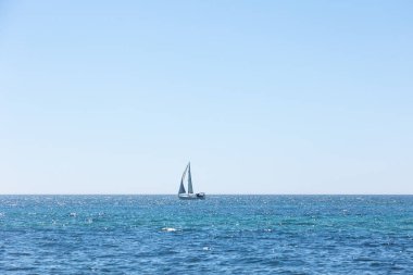 Sakin, mavi sularda, berrak bir gökyüzünün altında süzülen tek bir yelkenlinin minimalist fotoğrafı. Bu dingin deniz manzarası özgürlüğün, sükunetin ve deniz yaşamının özünü yansıtır. Seyahat ve deniz teması için idealdir. Algarve Portekiz