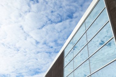 This image captures a modern building with large glass windows reflecting a bright blue sky filled with soft clouds. The sleek lines and minimalist design of the building contrast beautifully with the expansive sky clipart